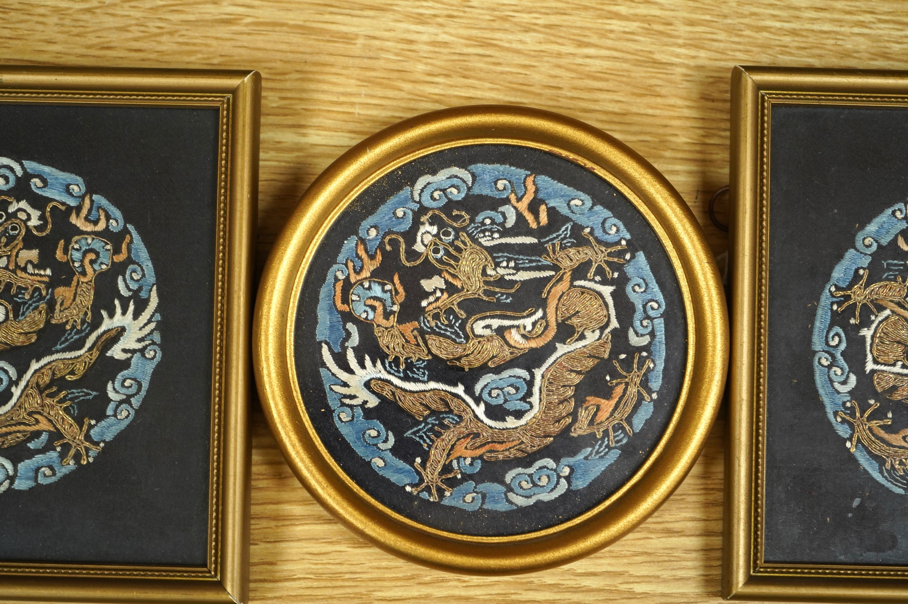 Three Chinese early 20th century embroidered roundels of five claw dragons, embroidered in gold thread and blue silk thread possibly symbolic motifs cut from a robe, embroidery 9cm diameter. Condition - embroidery good,